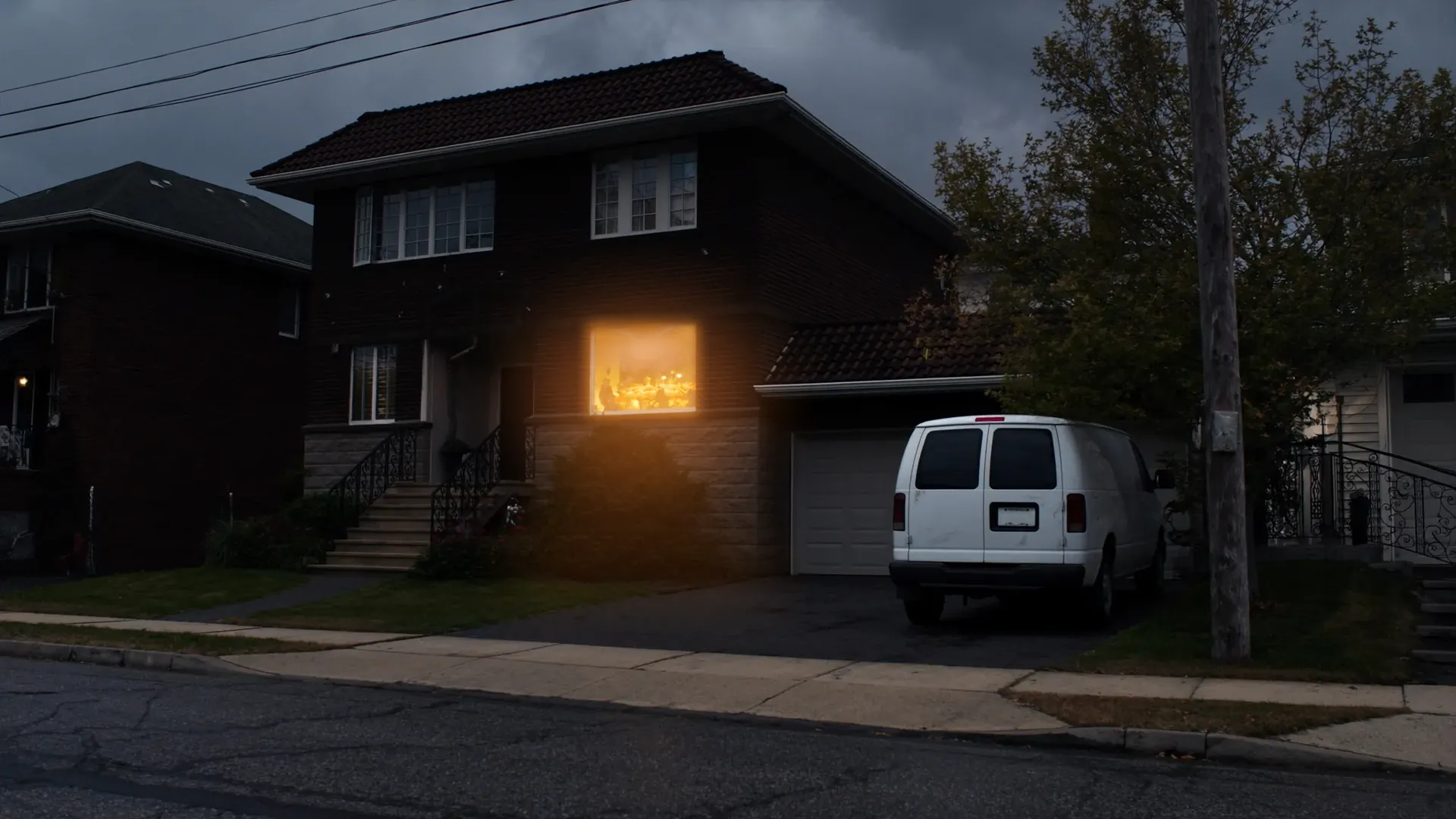 A brick house at dusk, a white van in the drive and the dining room window lit warm.